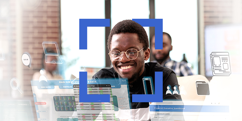 Smiling Black man with glasses at a desk, surrounded by translucent dashboards and icons in a collaborative office environment