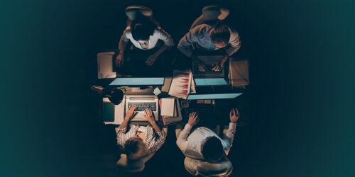 Top-down view of four people around a table working on laptops with documents and notebooks_autogenerated.