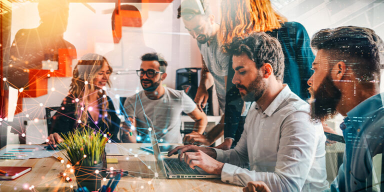 Diverse outsourced creative team collaborating around a table with a laptop, with a glowing data network overlay in the foreground.