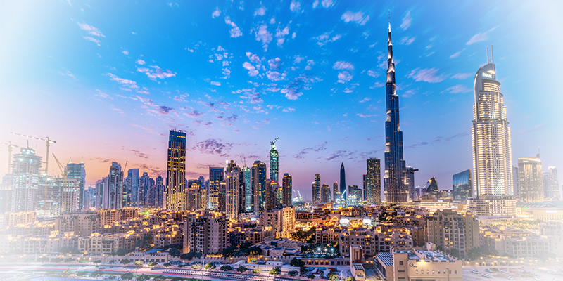 Panoramic skyline of Dubai at sunset with tall skyscrapers including Burj Khalifa, bathed in warm city lights