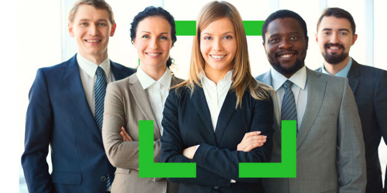 Five diverse business professionals posing together in an office, smiling confidently.