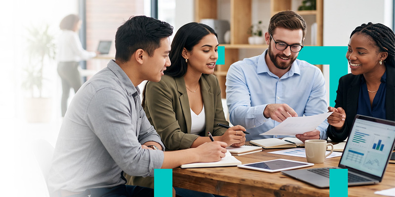 Group of four professionals collaborating at a table with documents and a laptop in a bright office.