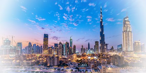 Panoramic skyline of Dubai at sunset with tall skyscrapers including Burj Khalifa, bathed in warm city lights