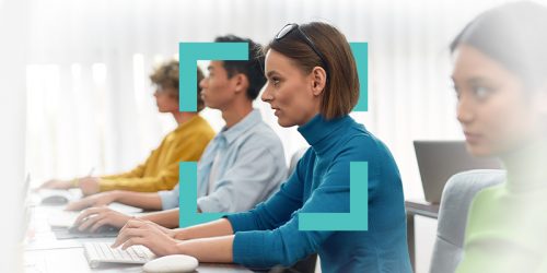 People seated at computers in a classroom training session, focused on work.Fixed lighting in a bright training room.