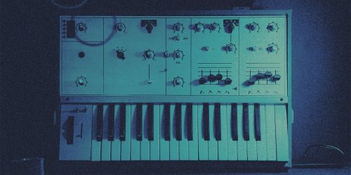 Vintage analog synthesizer with numerous knobs and a piano-style keyboard in a dimly lit room in a blue tint.