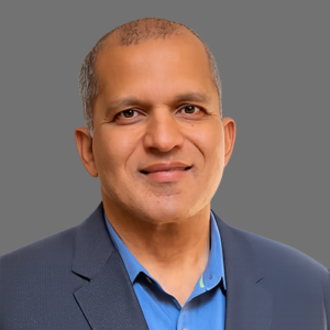 Professional head-and-shoulders portrait of a smiling middle-aged man wearing a blue shirt and navy blazer against a gray background.