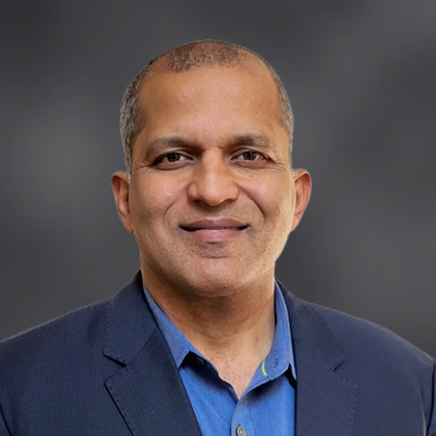 Portrait of a smiling man in a blue shirt and navy blazer against a gray studio background.