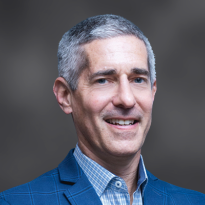 Professional headshot of a smiling middle-aged man with short gray hair in a blue blazer against a neutral background.